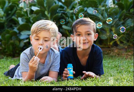 Nichts so schönes wie glückliche Kinder. Zwei entzückende Jungen spielen mit Blasen auf dem Gras im Hinterhof. Stockfoto