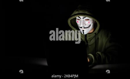 Anonymous in einer Haube tippt im Dunkeln auf einem Laptop. Stockfoto