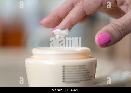 Die Handpflückcreme der älteren Frau mit dem Finger für die persönliche Hautpflege. Stockfoto