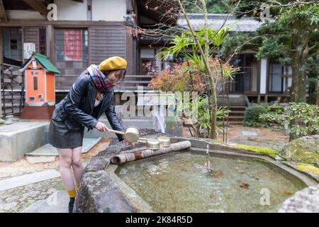 Ein hübsches japanisches Mädchen, das sich die Hände wäscht, wenn es einen Schrein oder Tempel besucht. Stockfoto