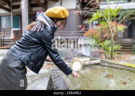 Ein hübsches japanisches Mädchen, das sich die Hände wäscht, wenn es einen Schrein oder Tempel besucht. Stockfoto