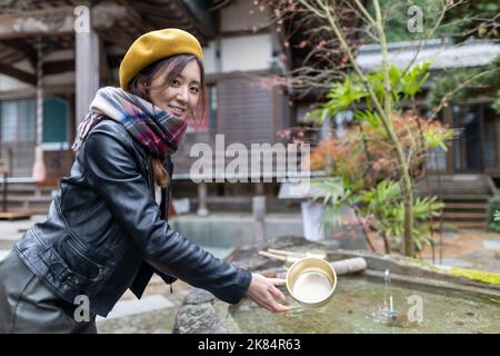 Ein hübsches japanisches Mädchen, das sich die Hände wäscht, wenn es einen Schrein oder Tempel besucht. Stockfoto