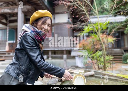 Ein hübsches japanisches Mädchen, das sich die Hände wäscht, wenn es einen Schrein oder Tempel besucht. Stockfoto