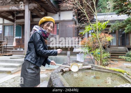 Ein hübsches japanisches Mädchen, das sich die Hände wäscht, wenn es einen Schrein oder Tempel besucht. Stockfoto