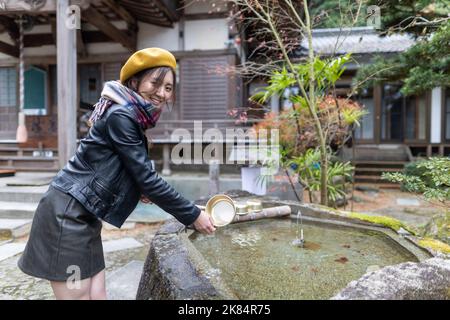 Ein hübsches japanisches Mädchen, das sich die Hände wäscht, wenn es einen Schrein oder Tempel besucht. Stockfoto