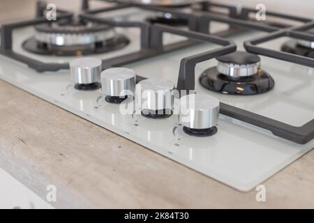 Moderner Gasherd aus gehärtetem Weißglas mit Erdgas oder Propan zum Kochen von Produkten auf einer leichten Arbeitsplatte im Kücheninnenraum.Industrie Stockfoto