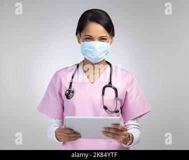Aufzeichnungen können einfach online gespeichert werden. Ein Porträt einer attraktiven jungen medizinischen Mitarbeiterin, die eine Maske und ein Stethoskop trägt, während sie sie benutzt Stockfoto