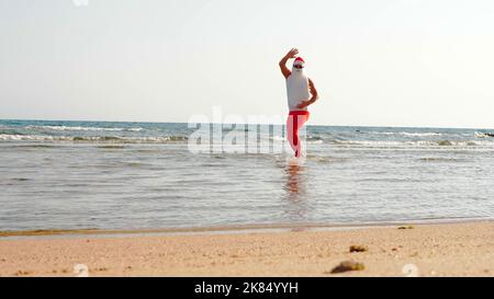 Witziger Weihnachtsmann. Vater Weihnachten, in Sonnenbrillen und Flossen, Spaß im Meerwasser in der Nähe des Sandstrandes. Weihnachtsmann Sommerurlaub. Hochwertige Fotos Stockfoto