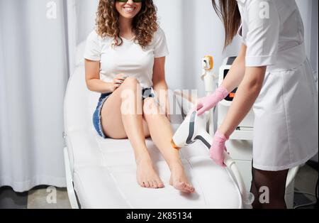 Beschnittene Ansicht einer lächelnden Frau, die sich einer Laserhaarentfernung bei der Kosmetikerin unterzogen hat. Salonpflege mit modernem Diodenlaser für perfekte glatte Haut. Stockfoto