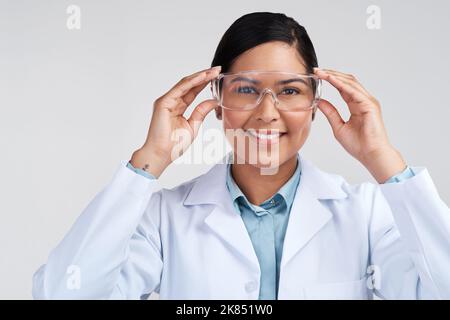 Sicherheit geht in meinem Labor an erster Stelle. Beschnittenes Porträt einer attraktiven jungen Wissenschaftlerin, die im Studio vor grauem Hintergrund eine Brille trägt. Stockfoto