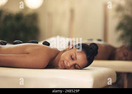 Buchen Sie sich einen Wellnesstag - Sie werden begeistert sein. Eine junge Frau bekommt eine Hot Stone Massage in einem Spa. Stockfoto