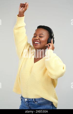 Nichts lässt mich so gut fühlen wie Musik. Eine junge Frau, die Kopfhörer trägt, während sie vor grauem Hintergrund tanzt. Stockfoto