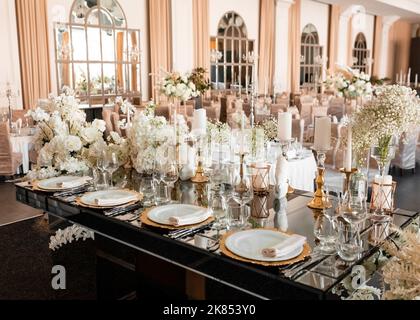 Seitenansicht des hübsch dekorierten Hochzeitsbanketttisches mit Blumenarrangements für frisch verheiratetes Paar. Moderne luxuriöse Hochzeitsdekoration in teuren Farbtönen Stockfoto