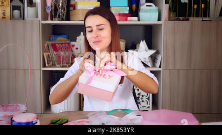 Geschenkverpackung. Attraktive Frau, Designer von Geschenken und Dekorationen zeigt Training online, zeichnet Videoblog, Webinar, sitzt vor dem Smartphone, Kamera. Online-Verkauf. Hochwertige Fotos Stockfoto