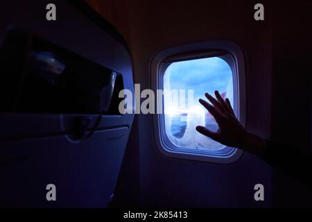 Weibliche Hand berührt die warmen Sonnenstrahlen vom Flugzeugfenster. Frau freut sich auf die Reise in ihren Urlaub. Mädchen auf einer Reise Flug sitzen in Stockfoto