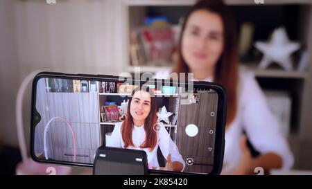 Geschenkverpackung. Attraktive Frau, Designer von Geschenken und Dekorationen zeigt Training online, zeichnet Videoblog, Webinar, sitzt vor dem Smartphone, Kamera. Online-Verkauf. Hochwertige Fotos Stockfoto