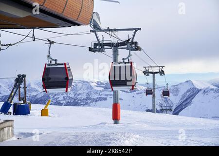 Gondelbahn im Skigebiet mit verschneiten Bergen im Hintergrund. Moderner Skilift mit Funitels und Stütztürmen hoch in den Bergen Stockfoto
