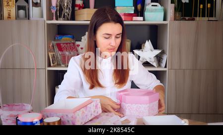 Geschenkverpackung. Attraktive Frau, Designer von Geschenken und Dekorationen zeigt Training online, zeichnet Videoblog, Webinar, sitzt vor dem Smartphone, Kamera. Online-Verkauf. Hochwertige Fotos Stockfoto