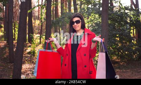 Frau mit Einkaufstaschen. Porträt einer attraktiven Frau mit farbigen Einkaufstaschen in den Händen, im Stadtpark. Einkaufen und Geschenke. Liefer- oder Spendenkonzept. Hochwertige Fotos Stockfoto