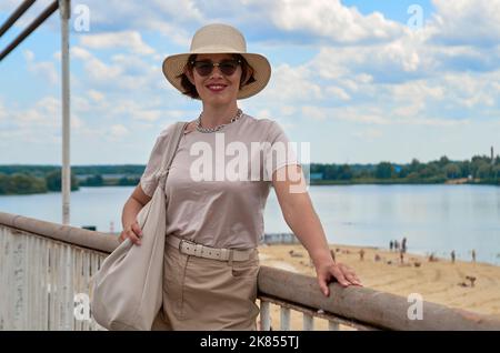 Porträt einer Reisenden Frau im Hut vor dem Hintergrund des Flusses und der Stadt Stockfoto