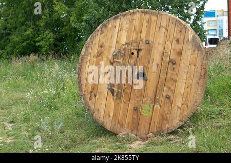 Auf einem grünen Rasen neben einer Baustelle liegt eine Holztrommel mit einem Kabel Stockfoto