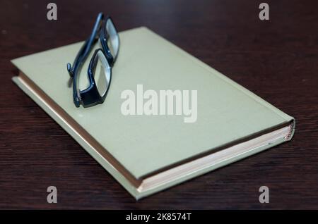 Ein geschlossenes Buch und Gläser liegen auf einer dunklen Holztischplatte Stockfoto