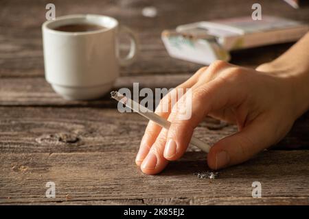 Eine Zigarette in den Händen eines Mädchens auf dem Tisch neben einer Tasse Kaffee, Zigaretten und Kaffee, schlechte Gewohnheiten, Rauchen Stockfoto