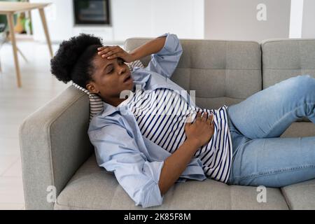 Kranke junge afroamerikanische Frau, die während der Menstruation gesundheitliche Probleme mit Kopf und Bauch hat Stockfoto