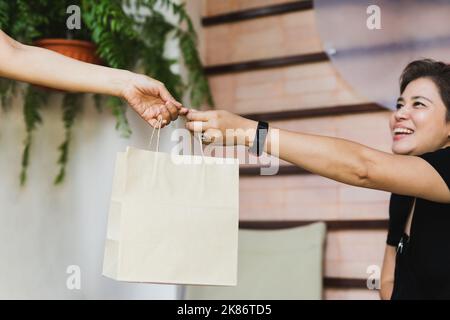 Die Kellnerin gab dem fröhlichen Kunden eine umweltfreundliche Papiertüte, die er im Café im Freien mitnehmen kann. Stockfoto