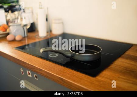 Bratpfanne auf modernem schwarzen Induktionsherd, Herd, Herdplatte oder eingebauter Kochplatte mit Keramikplatte im Kücheninnenraum aus Holz Stockfoto