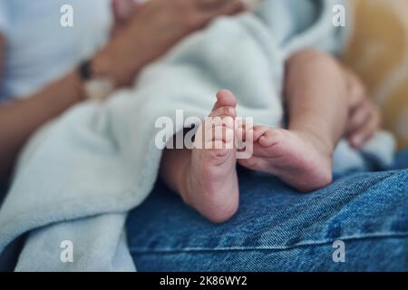 Ein paar Jahre in meinem Schoß, für immer in meinem Herzen. Eine unkenntliche Frau, die sich zu Hause mit ihrem Baby auf dem Sofa entspannt. Stockfoto