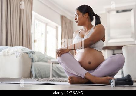 Yoga erleichtert die Beschwerden anderer Mütter im dritten Trimester. Eine schöne junge Schwangere, die zu Hause Yoga macht. Stockfoto