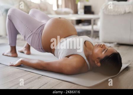 Regelmäßige Bewegung gibt mir mehr Energie und hilft mir, besser zu schlafen. Eine schöne junge Schwangere, die zu Hause Yoga macht. Stockfoto