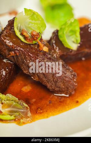 Köstliche Kalbsbacken in roter Sauce in der Nähe auf einem weißen Teller auf weißem Hintergrund Stockfoto