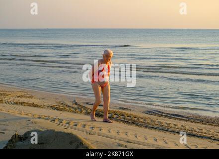 Juli 2022 Senigallia, Italien: Ältere Frau, die am Strand über das Sonnenuntergangsmeer und den Horizont läuft. Stockfoto