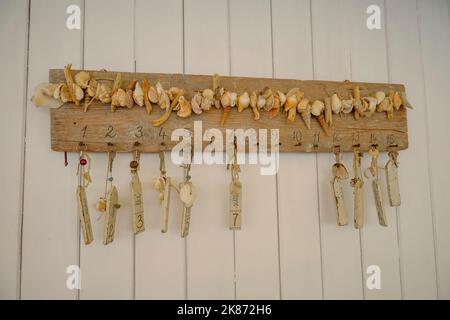 Zahlen und Schlüssel mit Anhängern auf einem Holzbrett mit Muscheln an der Wand. Resort, Hotel, Beach Club Stockfoto