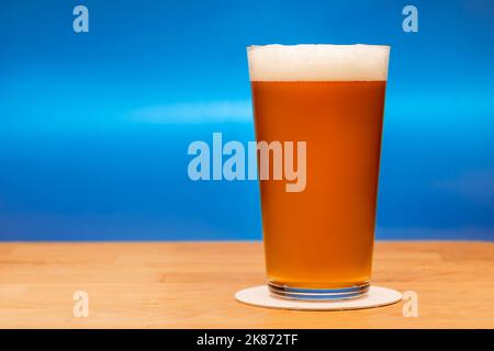 Volles Shaker Pint Glas Amber Ale oder Bier auf Holztisch mit grauem Hintergrund Stockfoto