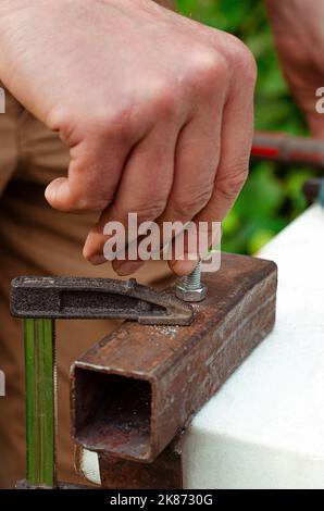 Eine Männerhand schraubt einen Bolzen in eine Metallmutter. Arbeiten mit Metall Stockfoto