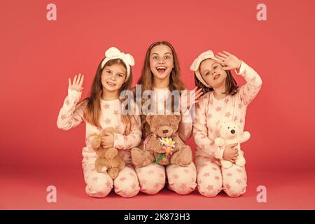 Hallo. Überraschte Kinder winken die Hände in Schlafanzug-Homewear. Mädchen sitzen zusammen mit Teddybären Stockfoto