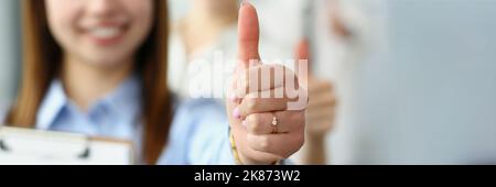 Lächelnde Frau zeigt Daumen nach oben und bestätigt den Erfolg an der Kamera Stockfoto