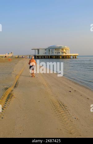 Juli 2022 Senigallia, Italien: Älterer Mann, der mit einem Stock in Richtung Rotonda al Mare am Strand über Meer, Sonnenaufgangshimmel und Horizont geht Stockfoto