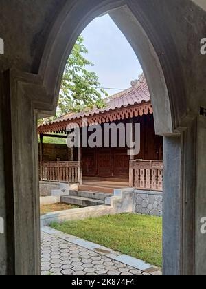 Vorderansicht eines traditionellen javanesischen Holzhauses, eingerahmt von einem Betontor Stockfoto