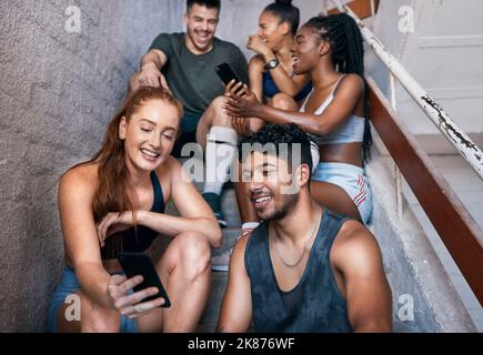 Fitness, Telefon und eine Gruppe von Freunden auf der Treppe Networking auf Social Media nach dem Training im Fitnessstudio. Glücklich, lächeln und Sport Menschen sitzen und Stockfoto