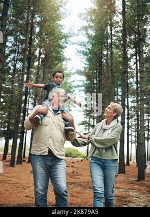 Wandern, Natur und Kinder mit älteren Pflegeeltern und ihrem Adoptivsohn gehen auf einem Sandweg durch die Bäume. Familie, Wandern und Kinder mit einem Stockfoto