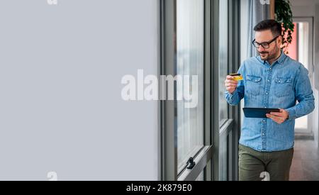 Bild eines erwachsenen Mannes in blauem Hemd, der beim Gehen die Nummer von seiner Debitkarte abliest. Stockfoto