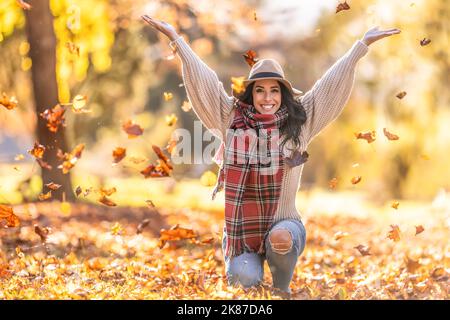 Eine glückliche junge Frau in einem Park wirft während eines indischen Sommers Blätter und genießt den Herbst. Stockfoto
