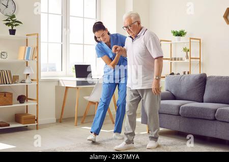 Krankenschwester in einer betreuten Wohnanlage, die einen älteren Patienten mit der Hand hält und ihm beim Gehen hilft Stockfoto