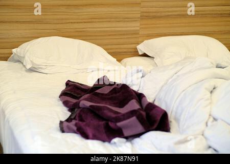 Das Bett war mit Kissen und einer gekrümmten Decke ausgestattet. Zerbröckelte Decke und Kissen auf leerem, zerknittertem Bett im Hotelzimmer nach dem Schlafen in der Nacht. Stockfoto