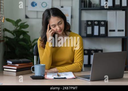 Gestresste asiatische Geschäftsfrau sorgt sich mit vielen Dokumenten auf dem Schreibtisch im Büro Stockfoto