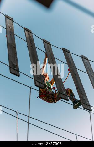 Im Abenteuerpark hängt ein erfahrener Bergsteiger an einer Wand aus Brettern Stockfoto